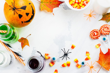 Halloween background with drinks, candies and decor on white table. Copy space. Top view