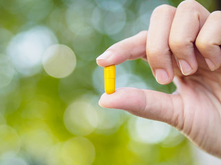 Closeup yellow pills in woman hand with bokeh background. Health care and medical concept.