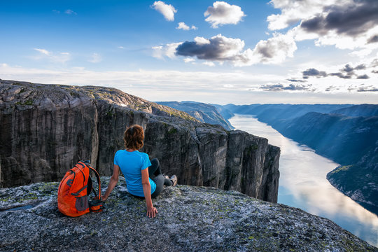 A woman is sitting on the edge of cliff on the way to boulder (Kjeragbolten) stuck in between the mountain crevices of Kjerag above a fjord, near Lysebotn, Norway. The feeling of complete freedom