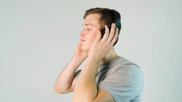Young man puts on his headphones and listening to music on white background