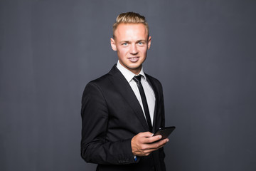 Happy business man in black suit typing sms on smartphone on grey