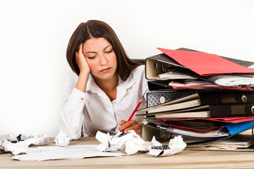 Mujer en la oficina agobiada junto a carpetas, cuadernos, papeles sobre una mesa escritorio de madera y fondo blanco. Vita de frente. Copy space