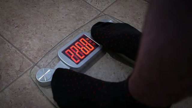Pair of male feet step onto modern digital weight scale - ALT ANGLE
