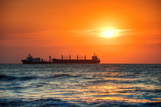 Sun setting at the sea with sailing cargo ship, sunrise view