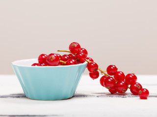 röda vinbärs klase i en turkos porslins skål på vit trä