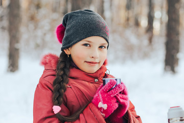 the little girl drinks hot tea in the winter forest.