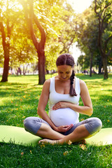 Charming pregnant woman holding belly while sitting in yoga pose