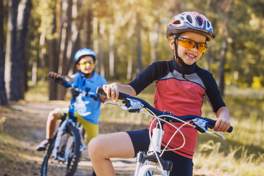 Kids On Abicycles In The Sunny Forest. Children Cycling Outdoors In Helmet