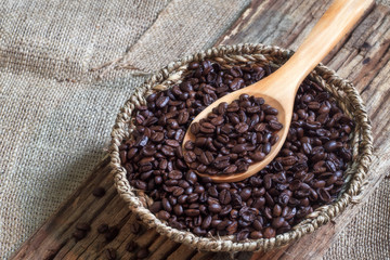 Coffee beans on wooden spoon over basket of coffee beans.