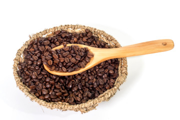 Coffee beans on wooden spoon over basket of coffee beans on white background.