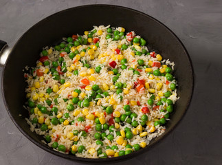 Frozen vegetables: corn, peas, tomatoes, carrots with rice in a frying pan.