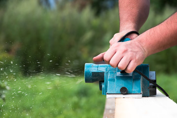 Close up hands of carpenter working with electric planer on wooden plank