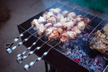 Grilled kebab cooking on metal skewers (grill). Roasted meat cooked at barbecue with smoke. Close up BBQ fresh pork meat chop slices. Traditional eastern dish, shish kebab.