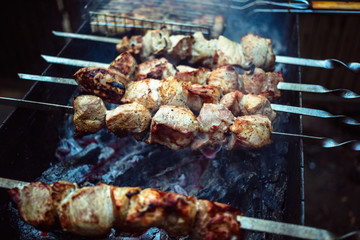Grilled kebab cooking on metal skewers (grill). Roasted meat cooked at barbecue with smoke. Close up BBQ fresh pork meat chop slices. Traditional eastern dish, shish kebab.