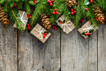 Christmas decorations on fir tree - gift boxes, holly and pine cones on wooden background, copy space