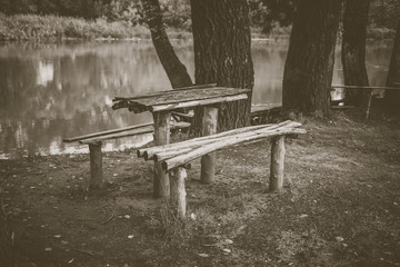 A wooden table and a bench on the river bank. A beautiful place to relax. Monochrome photo.