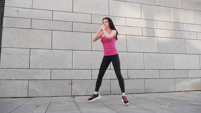 Happy young brunette fitness woman athlete making workout outdoors in the city on urban background in slow motion.