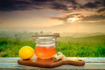 Alternative medicine with honey  and  ginger  on wooden table. Beautiful sunrise as background.