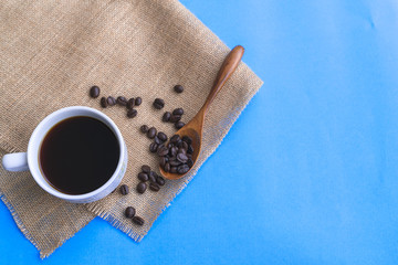 A cup of coffee and coffee bean grain on sack fabric put on blue background include copyspace for add text or graphic