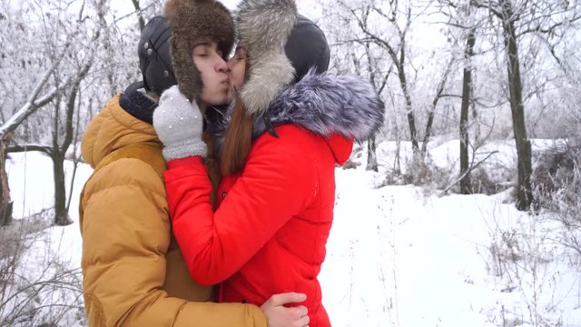Couple in love. Teenagers on a date in the winter outdoors. Girlfriend straightens his hat to her boyfriend and kisses him. Strong embrace.