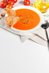Tomato soup with olive oil and herbs, with toasted bread, on white marble background, copy space