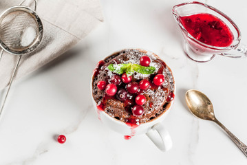 Winter, fall healthy breakfast or snack. The idea of a quick treat for Christmas. Chocolate mug cupkake in ceramic cup, with cranberry and sauce, powdered sugar. White marble table, copy space