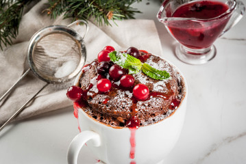 Winter, fall healthy breakfast or snack. The idea of a quick treat for Christmas. Chocolate mug cupkake in ceramic cup, with cranberry and sauce, powdered sugar. White marble table, copy space