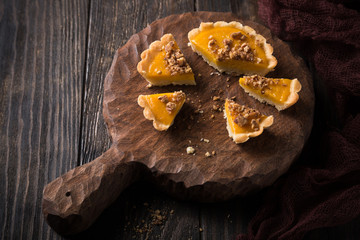 Pieces of pumpkin mini pie, tartlet made for Thanksgiving day on old wooden background. Healthy autumn food concept with copy space. Dark photo.