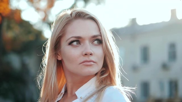 Portrait of young happy blonde student in the city. Slow motion. Beautiful girl in white sexy shirt in the street.