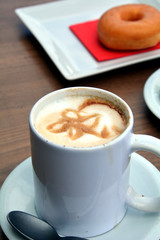 Cup of foamy cappuccino on a plate on a wooden table.