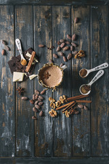 Vintage mug of hot chocolate, decor with nuts, caramel, spices. Ingredients above. Chopped dark and white chocolate, cocoa beans, anise over old wooden table. Top view with space. Dark rustic style