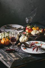 Autumn holiday table decoration setting with decorative pumpkins, apples, red leaves, empty plate with vintage cutlery, red wine, candle over wooden table. Rustic style