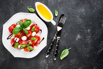 Caprese salad. Tomatoes, mozzarella cheese, tomatoes, olive oil, basil herb leaves, balsamic sauce on dark background. Italian food. Top view