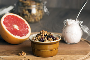 Granola from several types of cereals with nuts, coconut shavings and dried cranberries. Jar with homemade yogurt and grapefruit