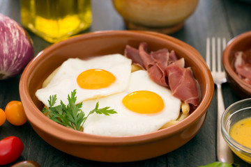 Fried eggs in a ceramic cup with spanish jamon for breakfast on a dark wooden background
