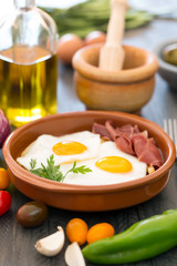 Fried eggs in a ceramic cup with spanish jamon for breakfast on black background