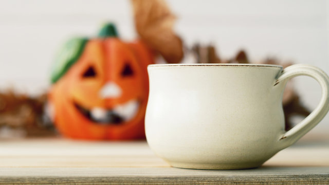 Picture of blurred pumpkie over wooden background with cup of tea or coffee in the front of it. Halloween  concept.
