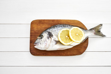 Fresh dorado fish with lemon on wooden cutting board on white wooden table. Top view, copy space