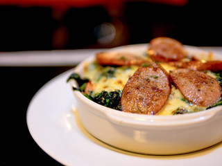 The selective focused and closeup image of braked spinach with cheese and sausage in a whit bowl.