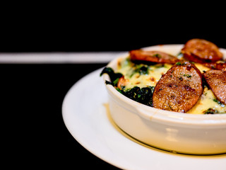 The selective focused and closeup image of braked spinach with cheese and sausage in a whit bowl.