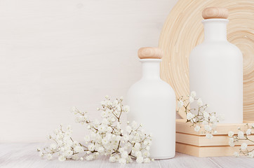 Blank white cosmetics bottles with small flowers on white wood board, copy space. Interior. Soft...