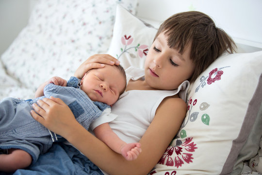 Beautiful boy, hugging with tenderness and care his newborn baby brother at home