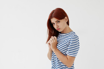 Isolated studio portrait of teenage girl in sailor shirt clasping hands on her chest and looking at camera with mournful and unhappy expression, feeling upset after break up with her boyfriend