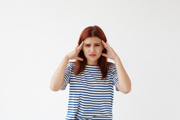 Student girl in sailor shirt frowning, looking at camera with painful expression and squeezing temples, having headache or migraine becuase of stress she experiencing during preparations to exams