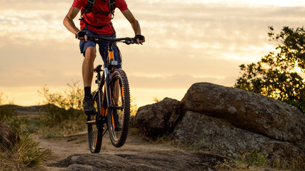 Fototapeta na wymiar Cyclist in Red Riding the Bike on the Rocky Trail at Sunset. Extreme Sport and Enduro Biking Concept.