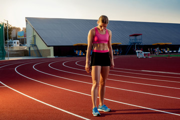 Picture of beautiful young European female runner or sprinter standing on outdoor stadium track,...