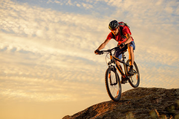 Naklejka na ściany i meble Cyclist in Red Riding the Bike Down the Rock at Sunset. Extreme Sport and Enduro Biking Concept.