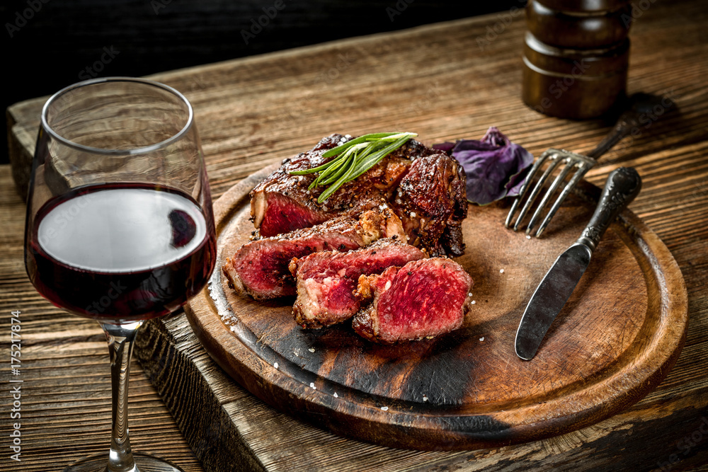 Wall mural grilled ribeye beef steak with red wine, herbs and spices on wooden table