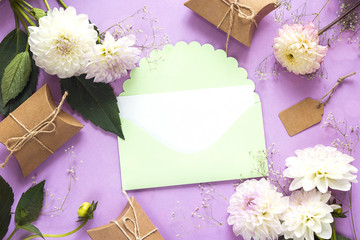 Empty green envelope with dahlias and gift boxes on a violet background. Copy space.