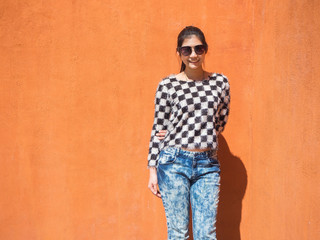 Obraz premium Woman wear sunglasses and standing posing outdoors,girl wearing black and white shirts are smiling happily on orange background